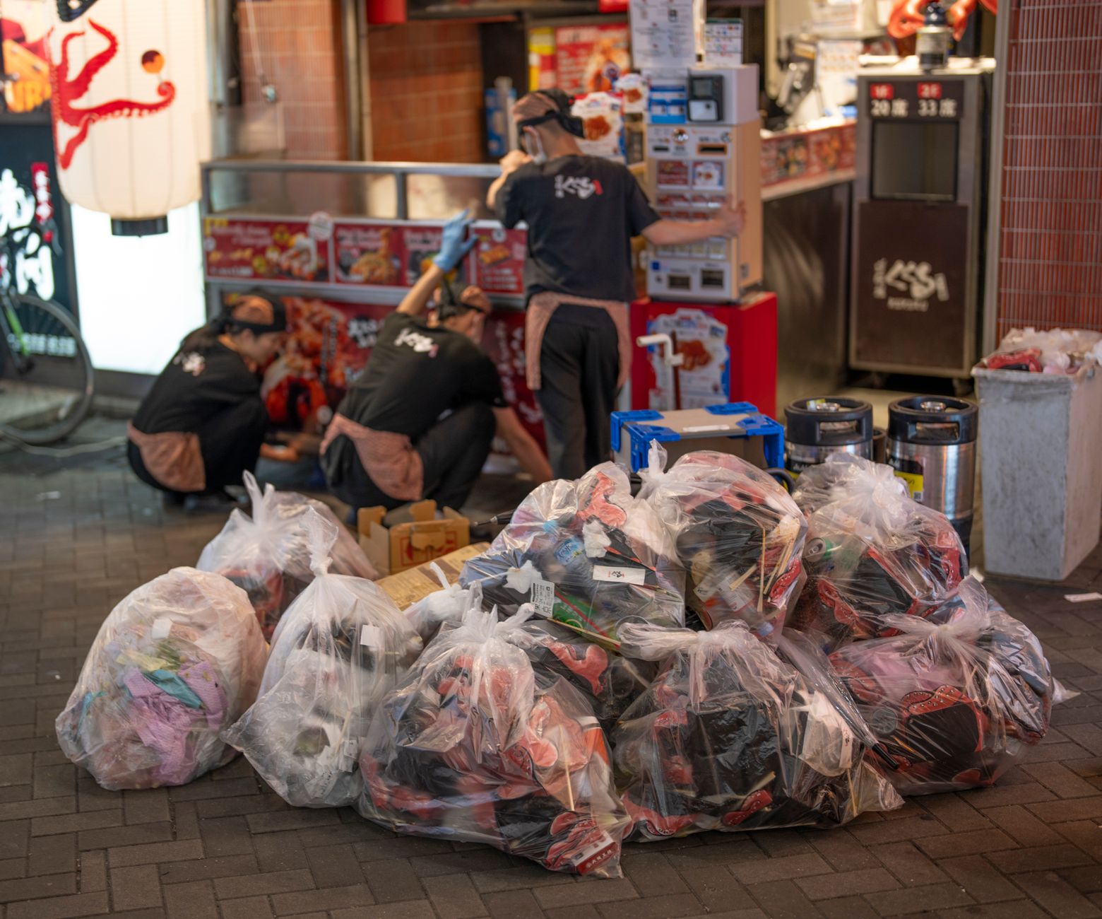 What a Garbage Day Looks Like in an Osaka Apartment — shared metal garbage collection rack outside a small Osaka apartment building with clear plastic bags and protective mesh net